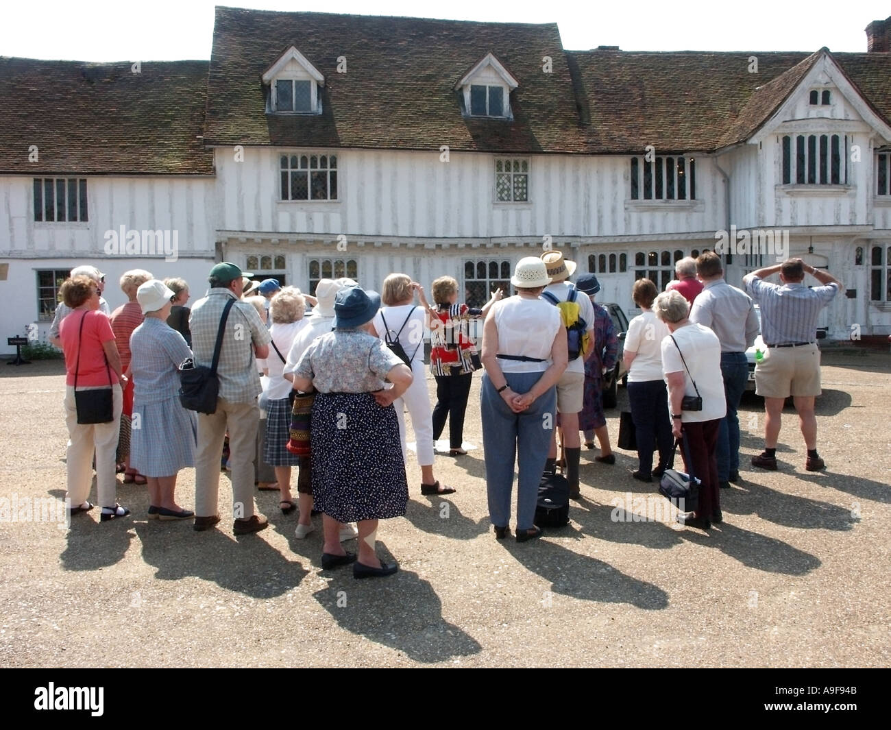 Groupe de touristes debout écoutant les guides parler de l'historique Jettied bâtiment Guildhall à ossature en bois Lavenham Suffolk East Anglia Angleterre Royaume-Uni Banque D'Images