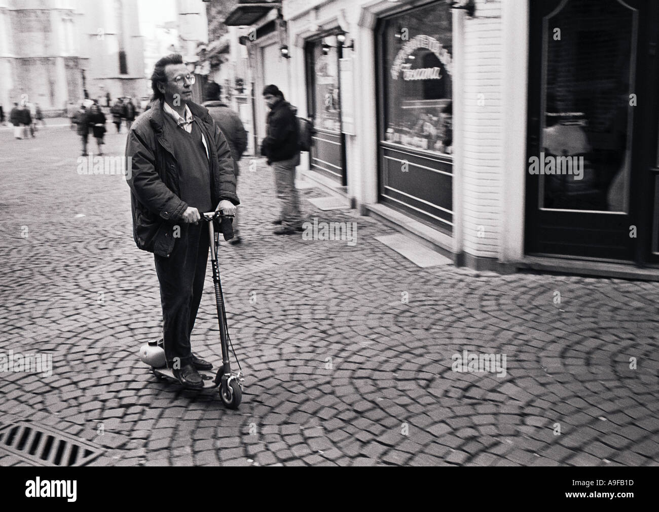 Le noir et blanc d'un homme monté sur un micro scooter essence à travers le centre d'Anvers en Belgique en 1995 Banque D'Images