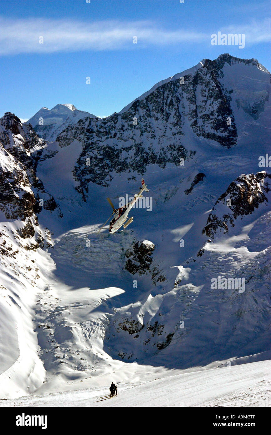 Trois skieurs à faire leur chemin à travers une piste là-haut, dans les montagnes avec un hélicoptère volant au-dessus d'eux à ski piste Corvatsch Banque D'Images