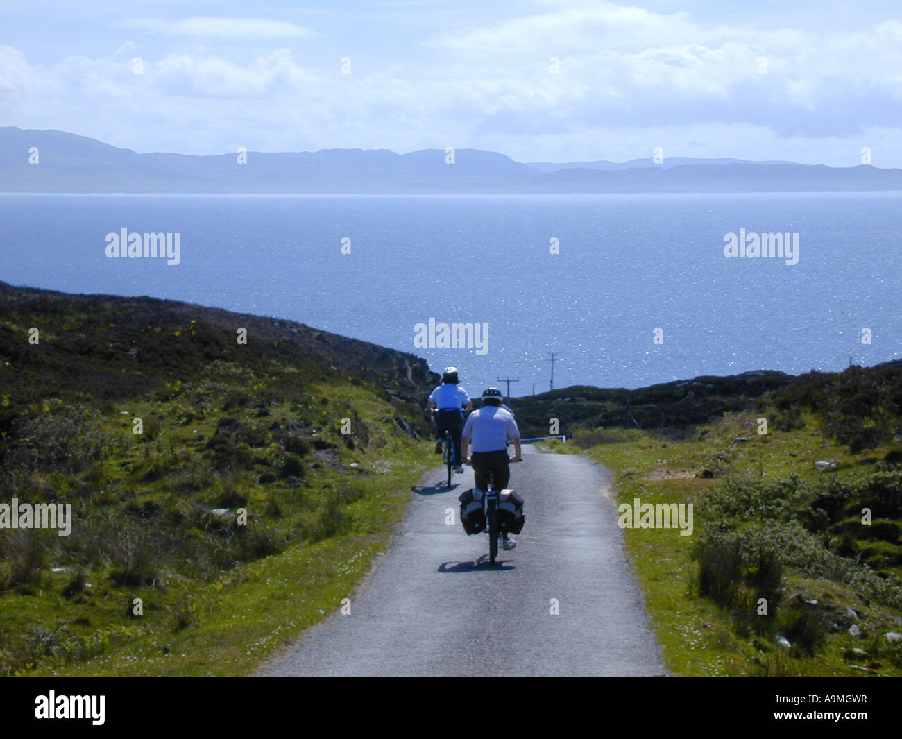 Deux cyclistes sur une route goudronnée sur l'île de Colonsay avec l'île de Jura en arrière-plan Banque D'Images
