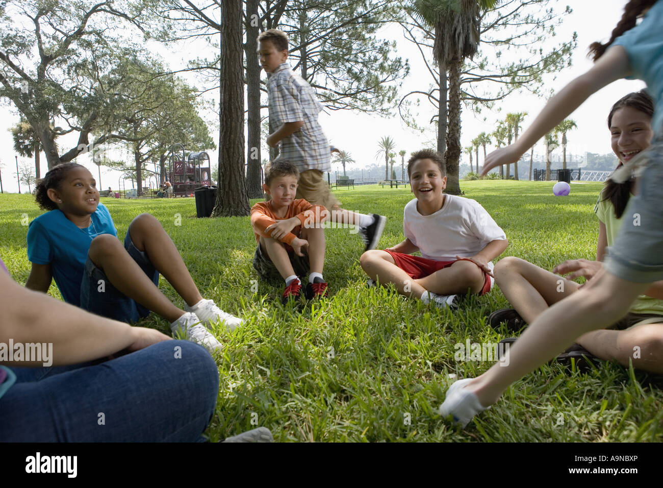 Les enfants, assis en cercle sur l'herbe avec leur enseignant, tandis qu'un garçon et agirl courir autour d'eux Banque D'Images