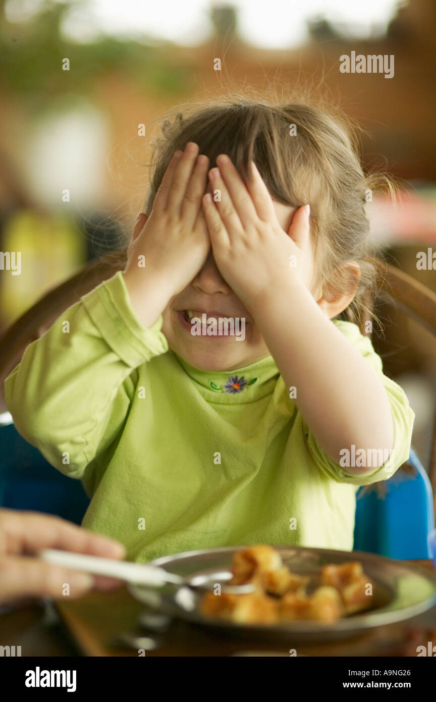 Portrait d'un enfant couvrant ses yeux alors qu'elle est sur le point d'être nourris cuillère Banque D'Images