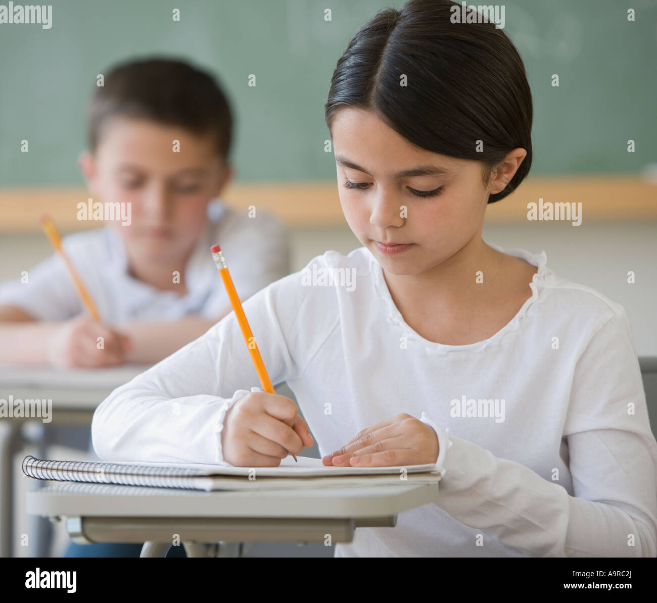 Girl writing at desk in classroom Banque D'Images