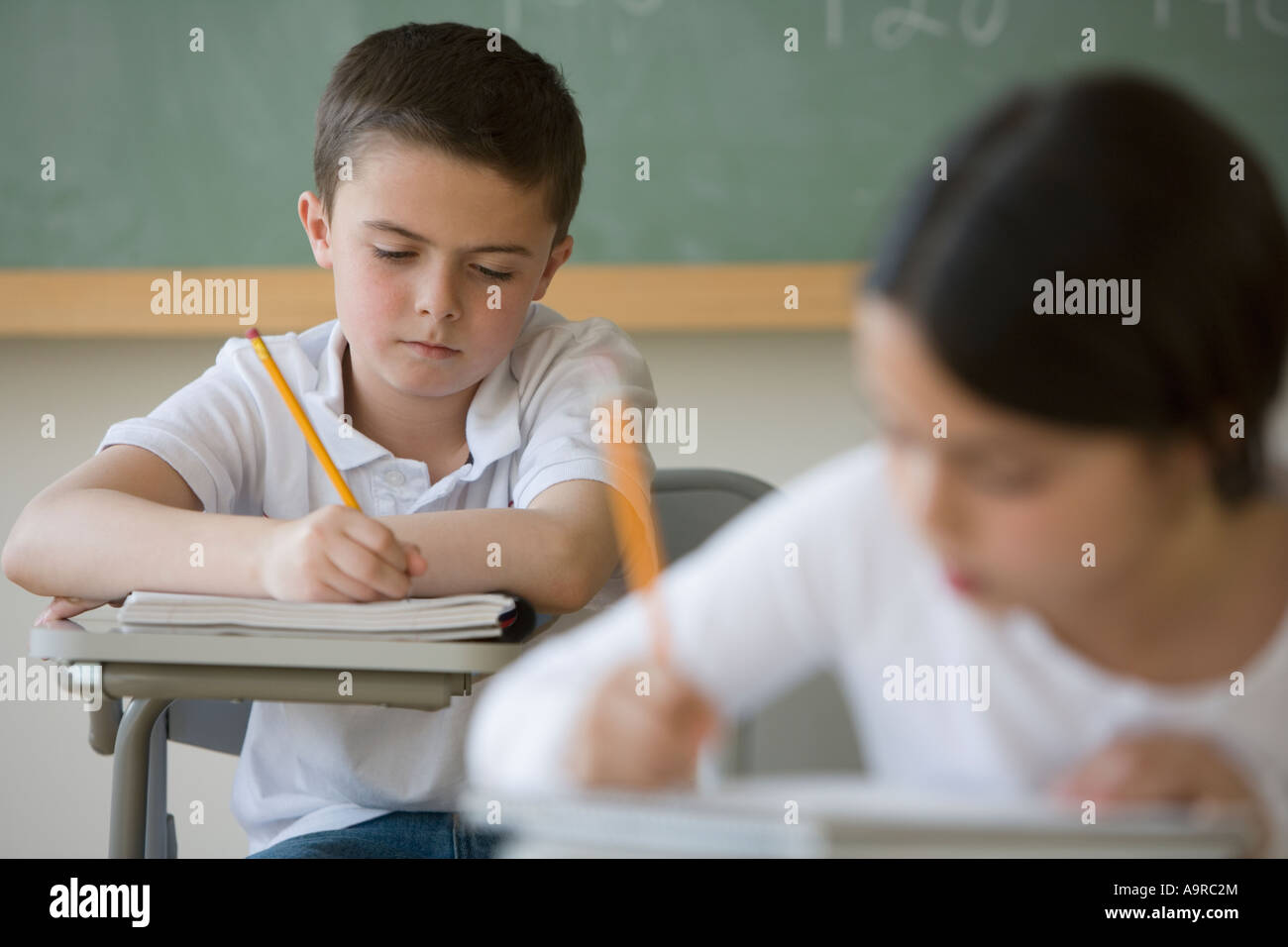 Garçon écrit at desk in classroom Banque D'Images