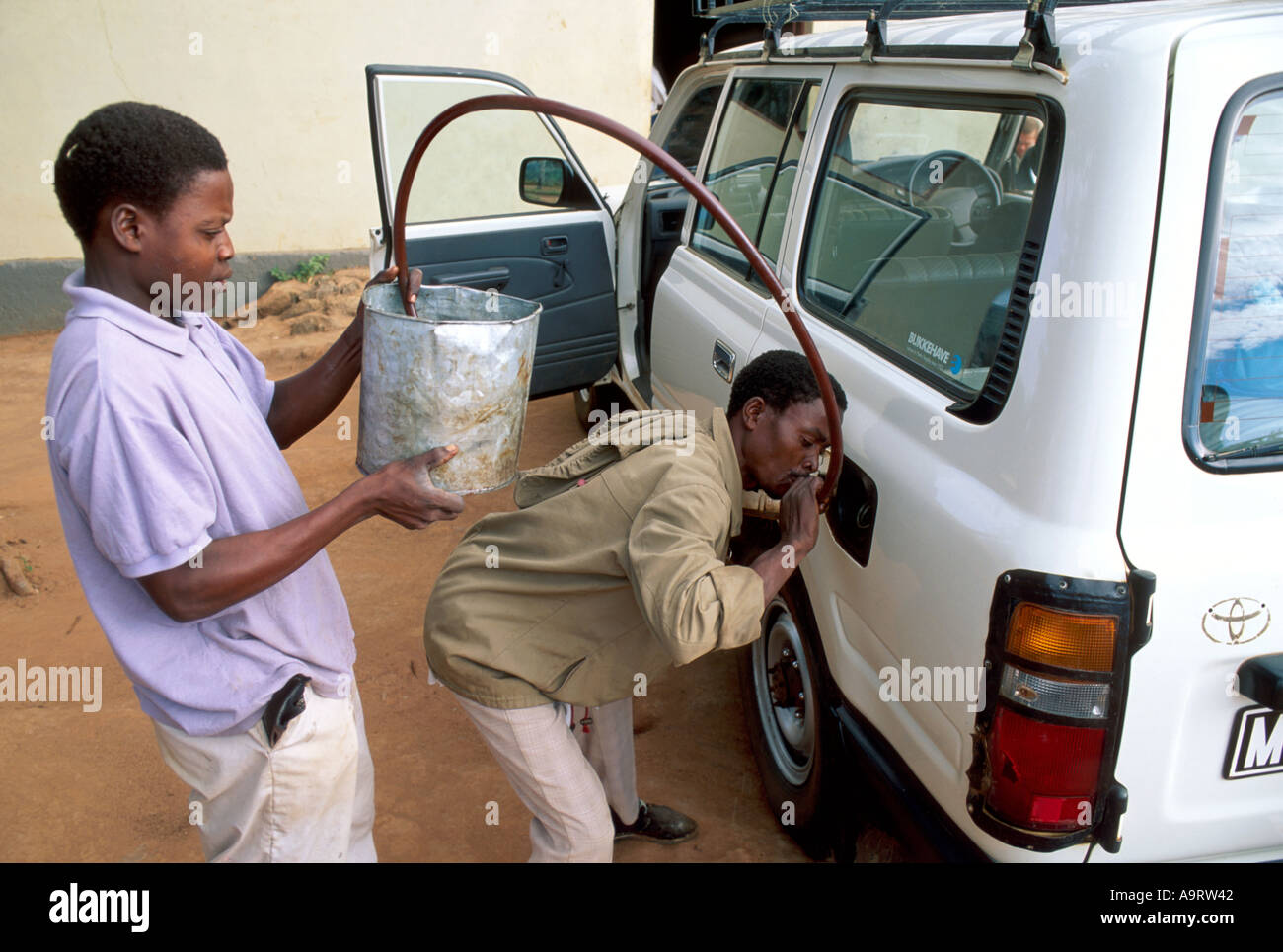 Jeunes entrepreneurs qui vendent du diesel en bord de route en aspirant le carburant d'un seau dans un véhicule à 4 roues motrices. Zambezia, Mozambique Banque D'Images