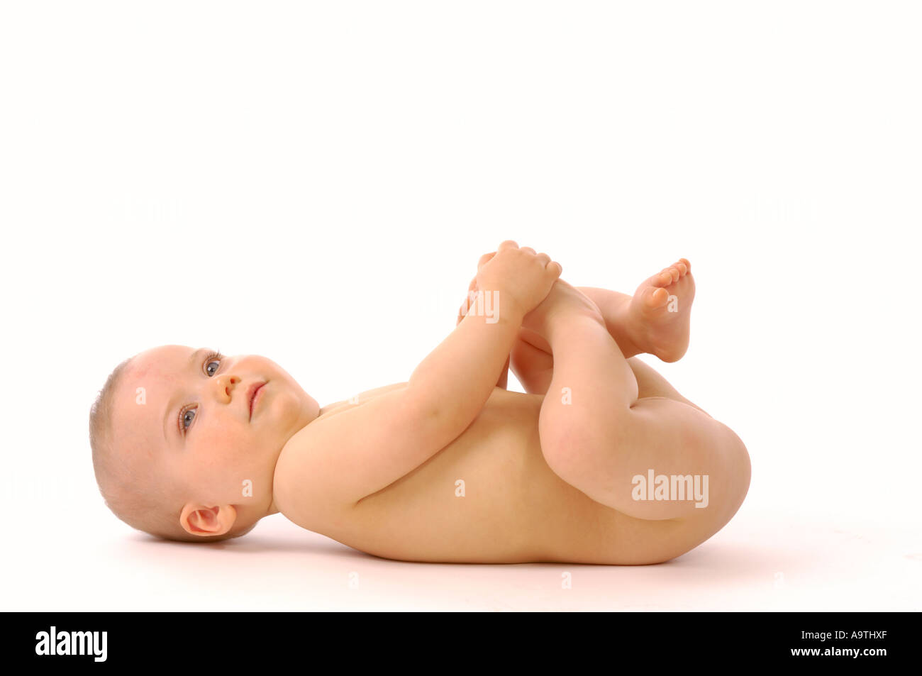 Vue de côté d'un bébé caucasien sans couche couchée sur un fond blanc jouant avec ses pieds. Banque D'Images Vue de côté d'un bébé caucasien sans couche couchée sur un fond blanc jouant avec ses pieds. Banque D'Images