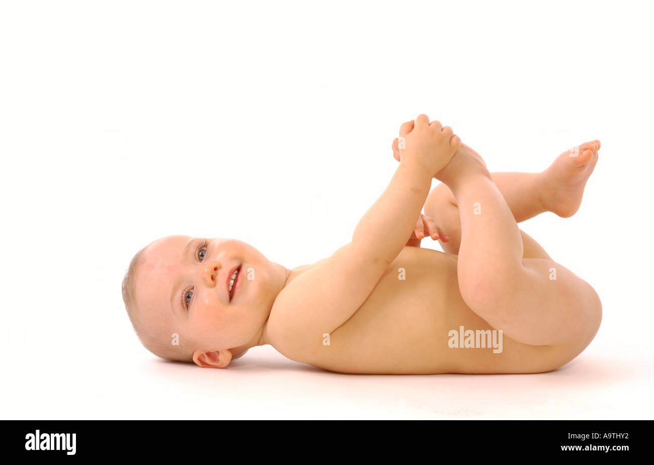 Vue de côté d'un bébé caucasien sans couche couchée sur un fond blanc jouant avec ses pieds. Banque D'Images Vue de côté d'un bébé caucasien sans couche couchée sur un fond blanc jouant avec ses pieds. Banque D'Images
