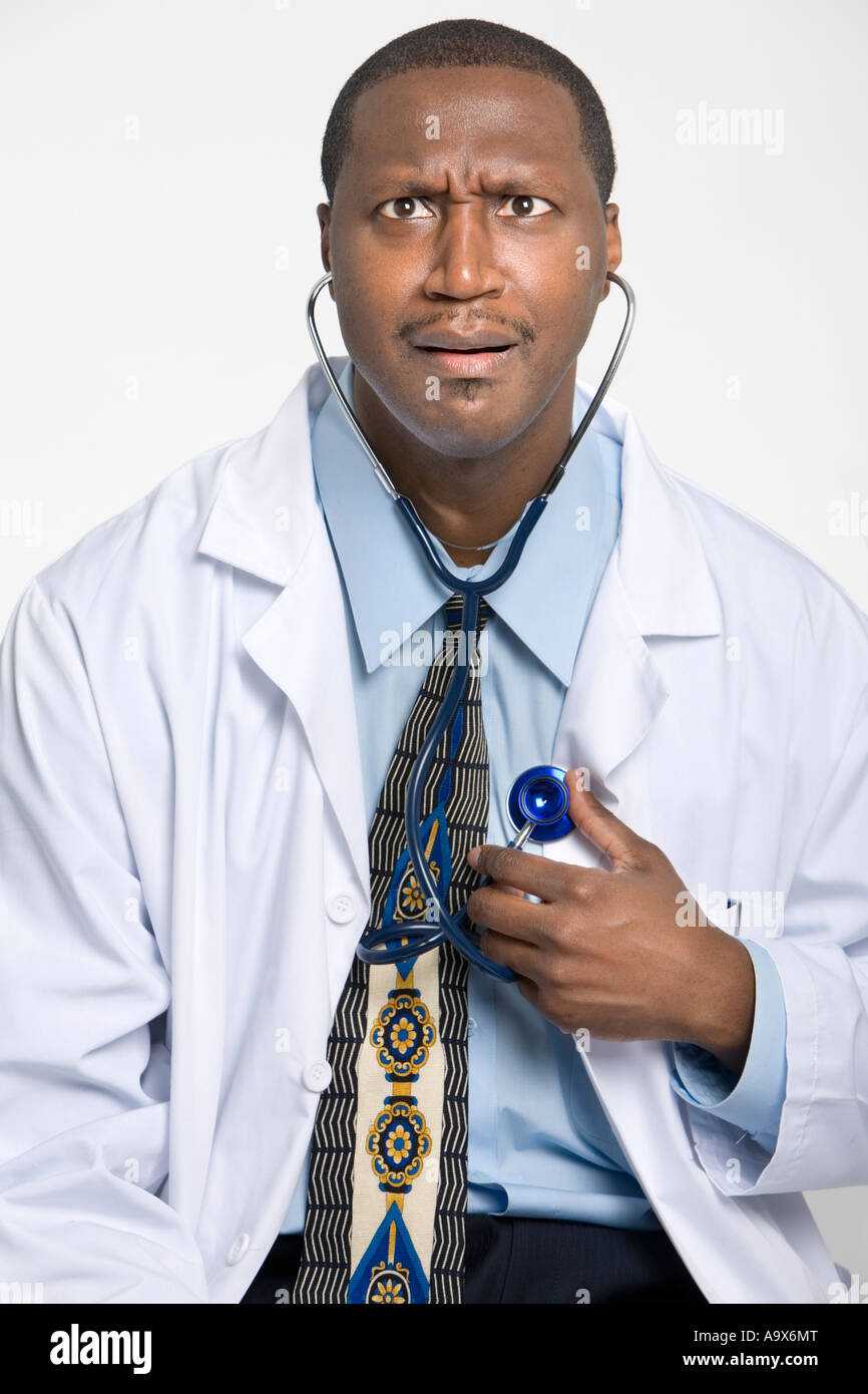 Photo d'humour d'un médecin à l'écoute de son propre cœur avec un stéthoscope faisant un drôle de visage et portant un manteau blanc Banque D'Images