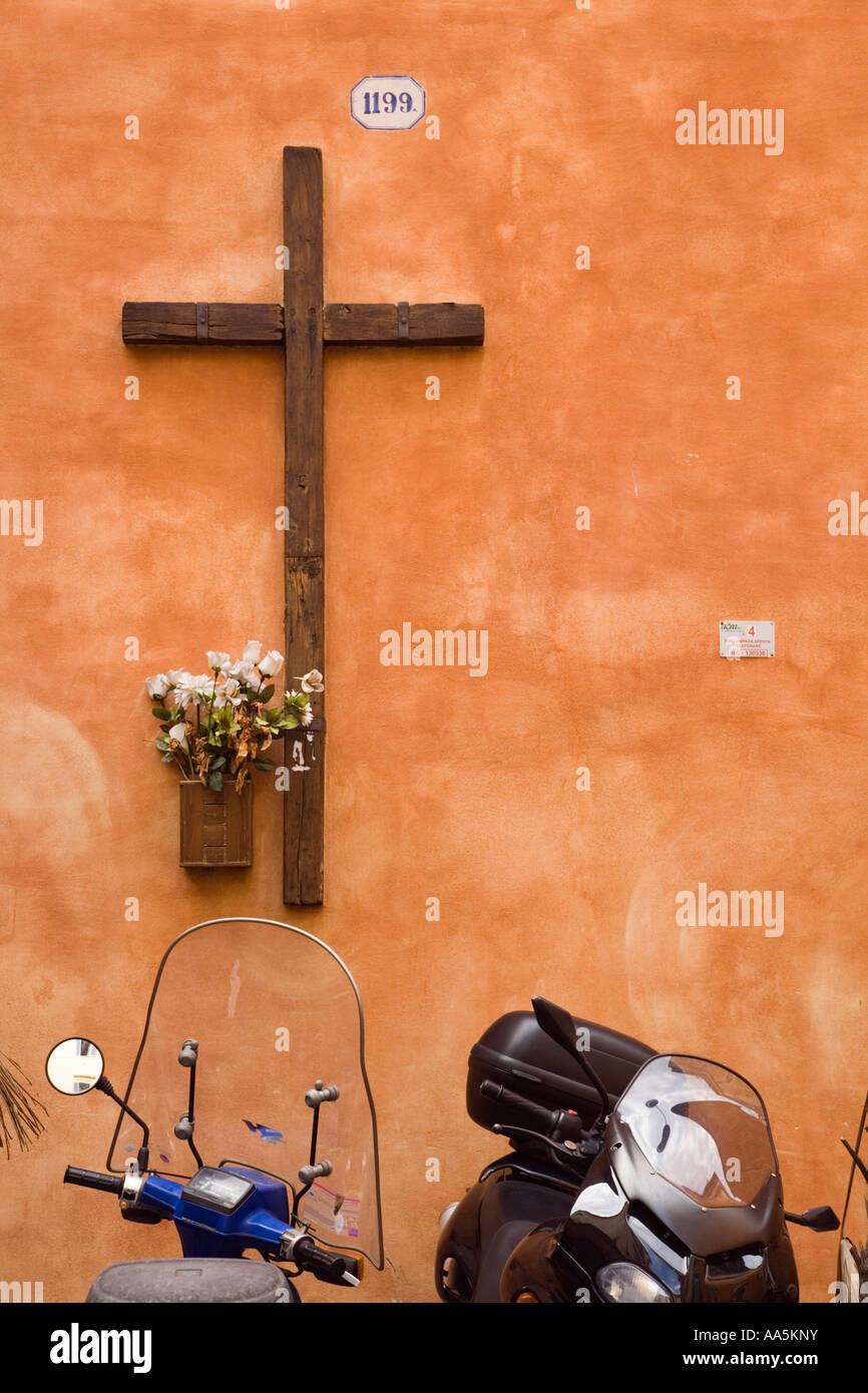 Italie Rome motos et scooters garé à l'extérieur de l'église avec croix de bois fixé sur mur ocre Banque D'Images