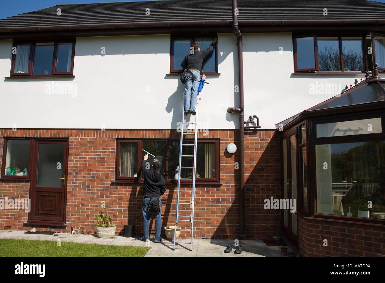 Le Nord du Pays de Galles avril, deux jeune homme sur une échelle nettoyage du premier étage se tenant sur le sol de windows windows cuisine nettoyage Banque D'Images
