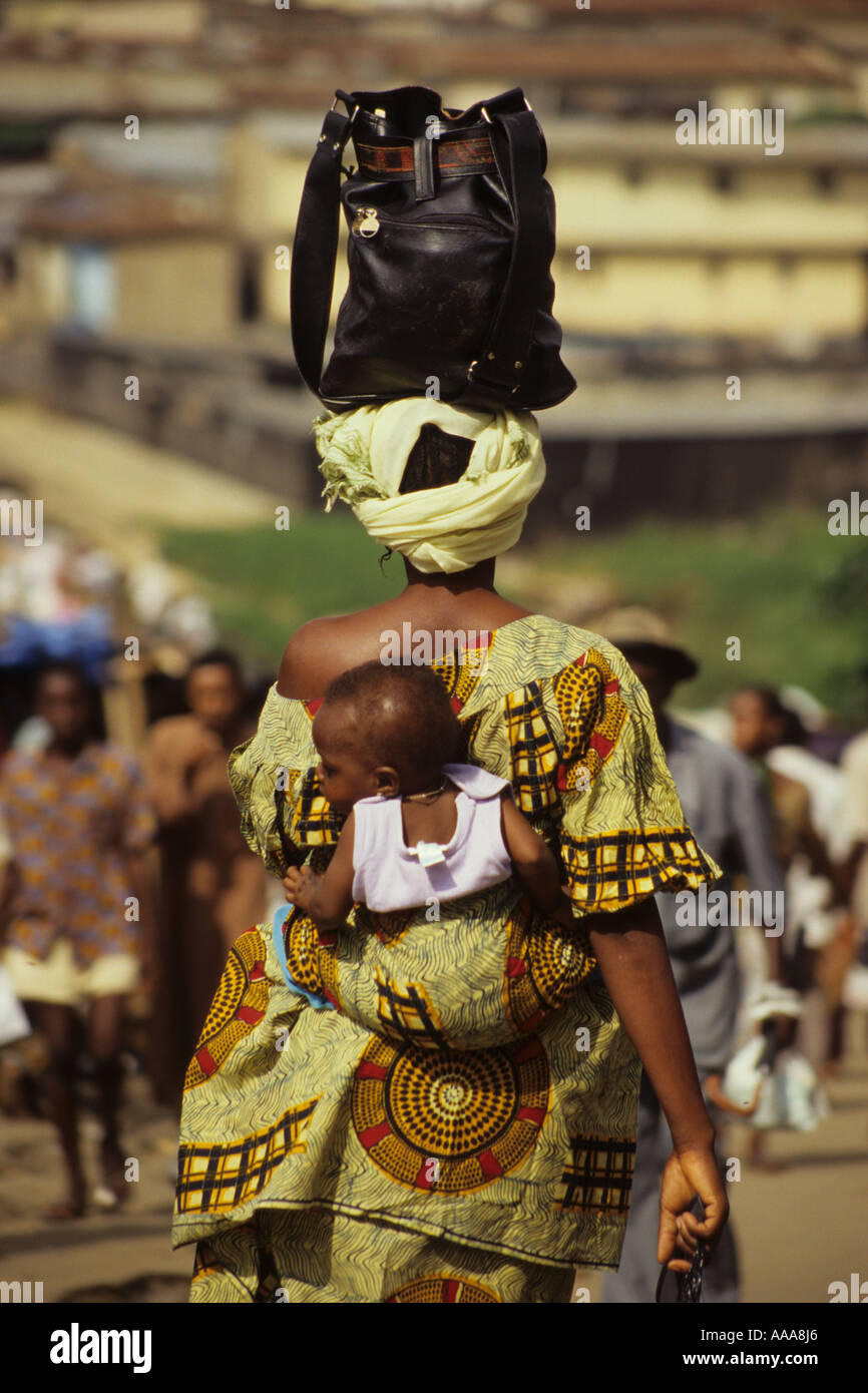 Abidjan, Côte d'Ivoire, Côte d'Ivoire, Afrique de l'Ouest. Femme ivoirienne exerçant son bébé sur le dos, sac à main sur la tête Banque D'Images