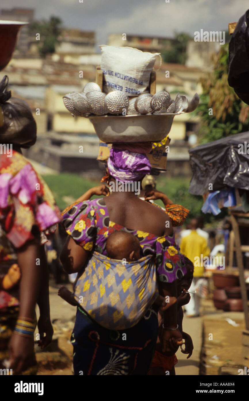 Abidjan, Côte d'Ivoire, Côte d'Ivoire, Afrique de l'Ouest. Mère ivoirienne avec bébé sur le dos, d'ustensiles de cuisine à vendre en tête de bassin, sur Banque D'Images