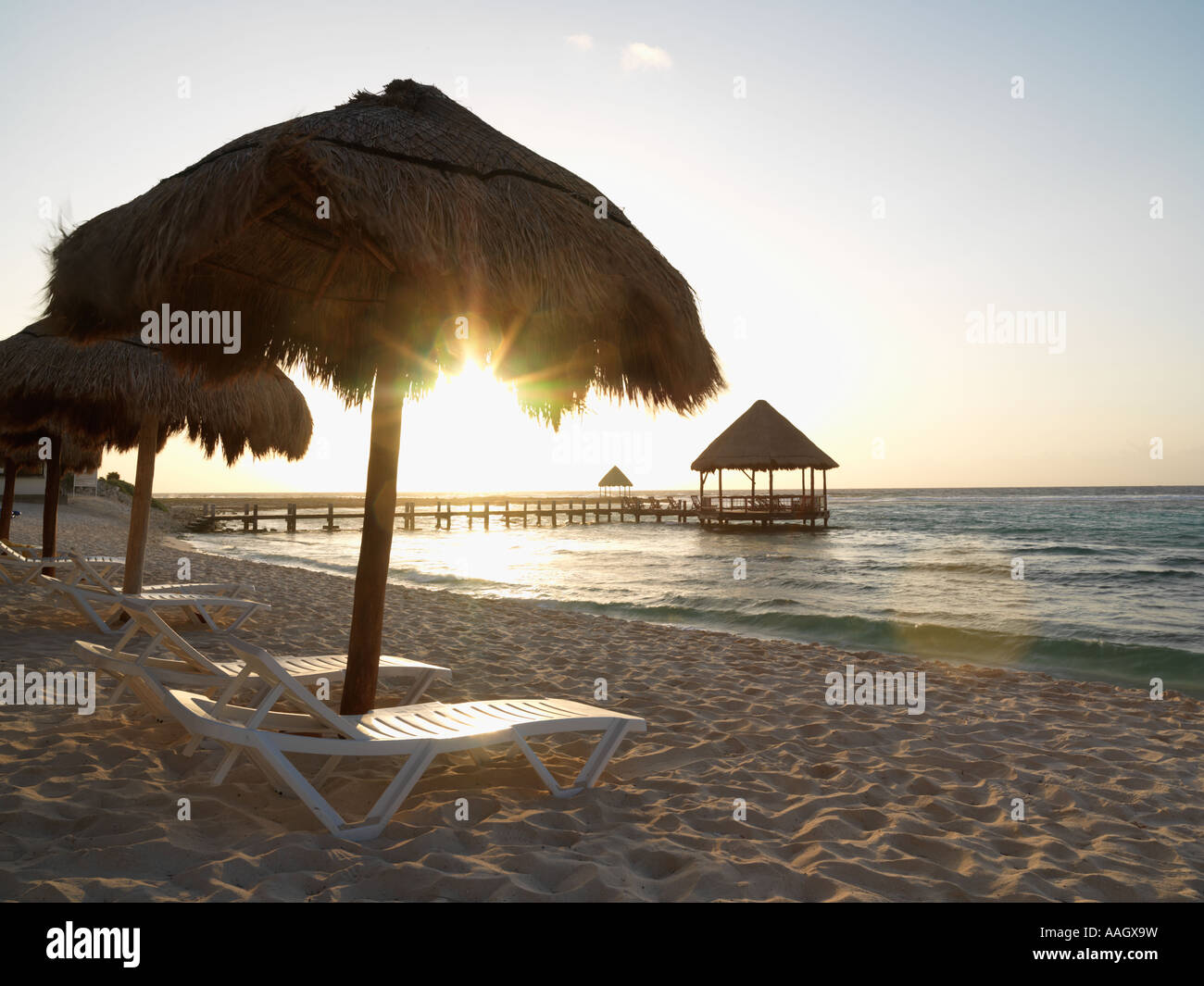 Le Mexique Péninsule du Yucatan Quintana Roo Cancun Riviera Maya chaises de plage sous des palapas au lever du soleil avec pier et palapa jutting ou Banque D'Images