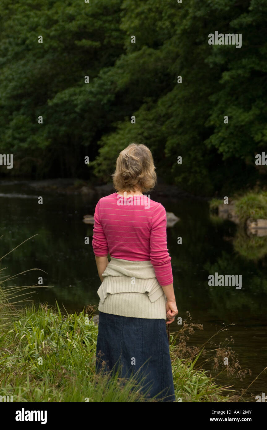 Cardigan rose woman standing by elle-même par l'observation de Rheidol rivière le débit d'eau lentement Banque D'Images