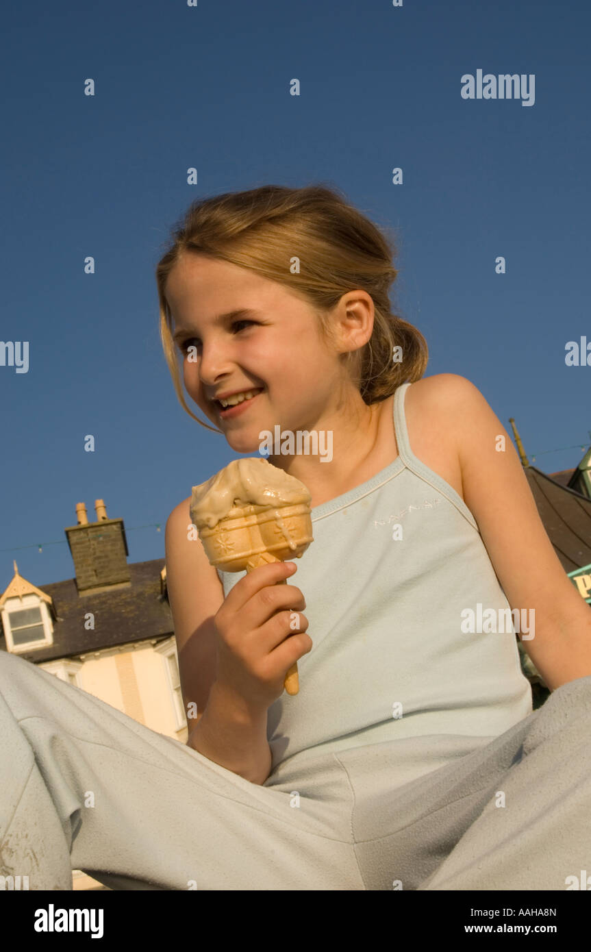 Smiling young huit 8 ans girl eating ice cream double cône sur la promenade d'Aberystwyth, Pays de Galles UK sur une chaude après-midi d'été Banque D'Images
