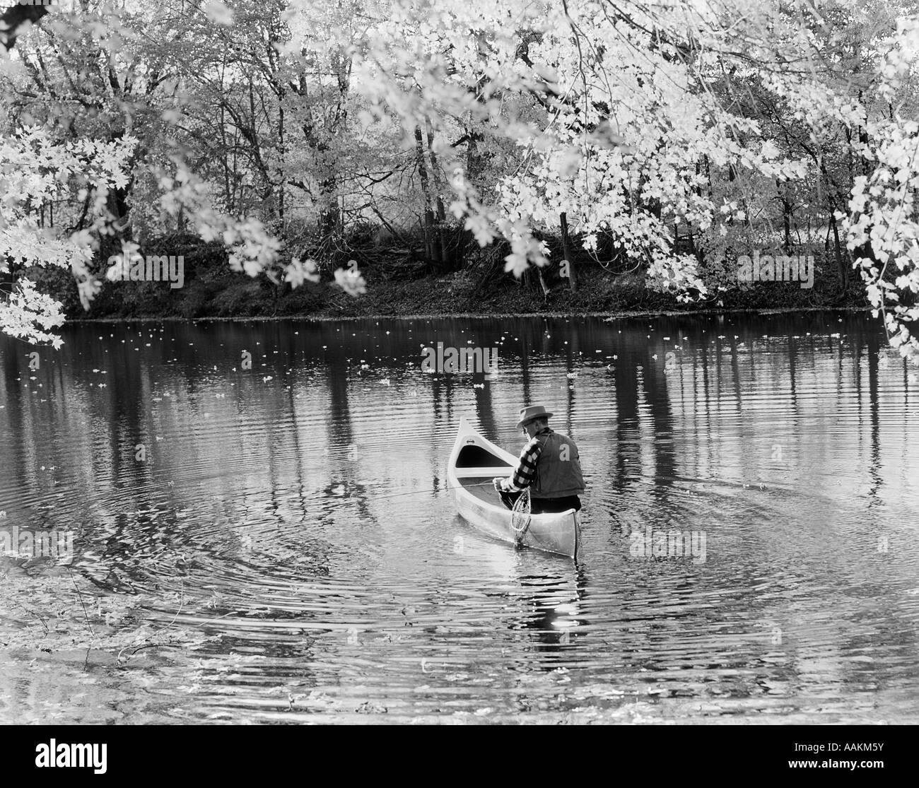 1970 VUE ARRIÈRE DE LA PÊCHE AU LARGE DE L'homme plus âgé du canoë DANS LE LAC Banque D'Images