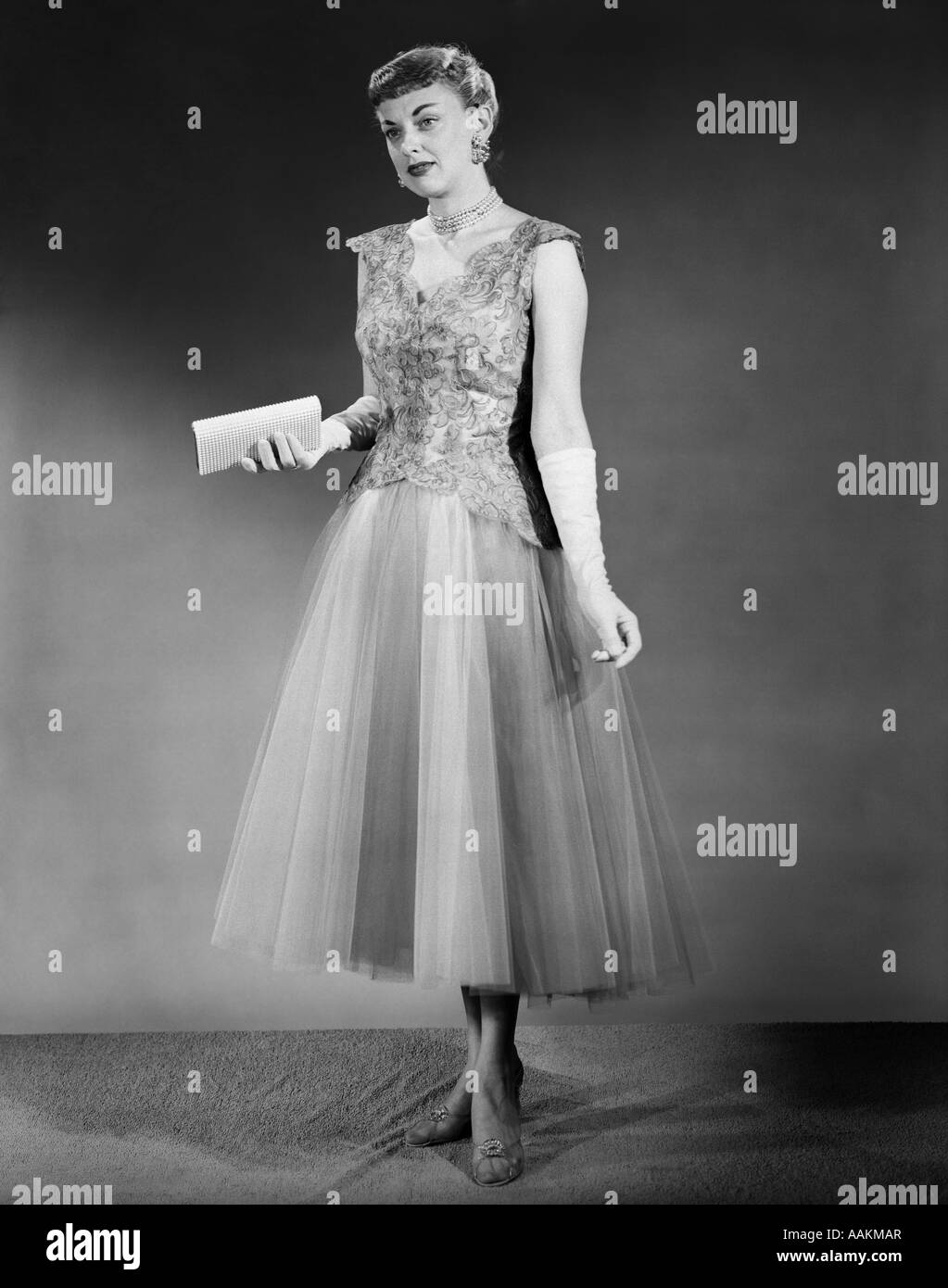 1950 Femme debout à l'intérieur portant robe de soirée formelle HOLDING POCKETBOOK Banque D'Images