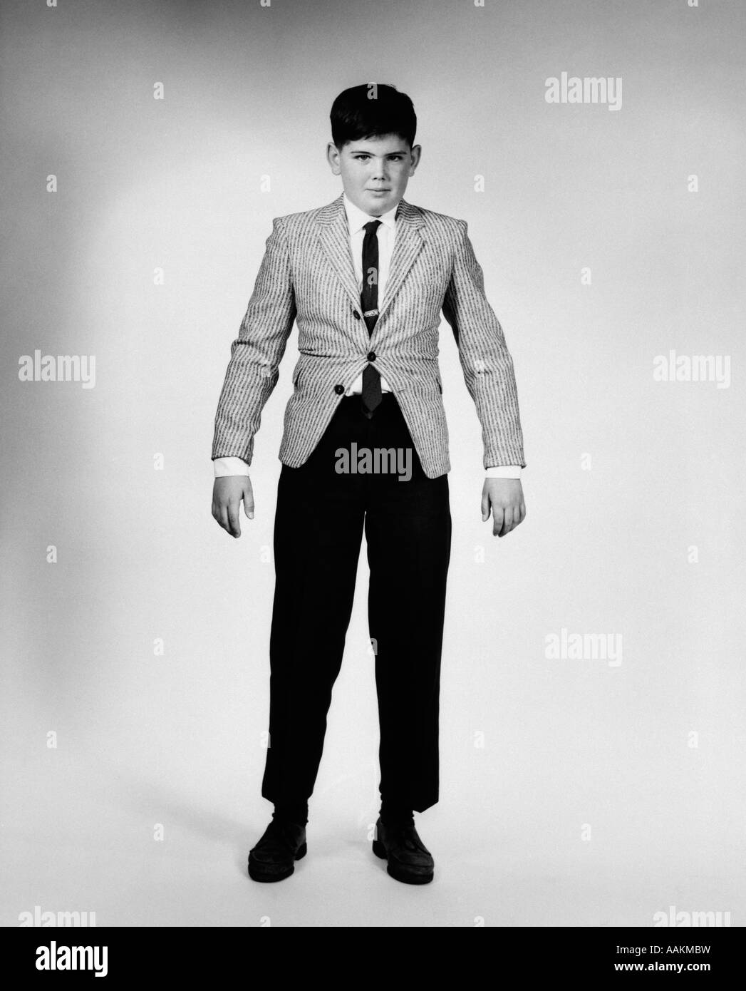 Années 1950 Années 1960 GARÇON ENVAHI PAR TROP SERRÉ en veste et pantalon de sport LOOKING AT CAMERA Banque D'Images