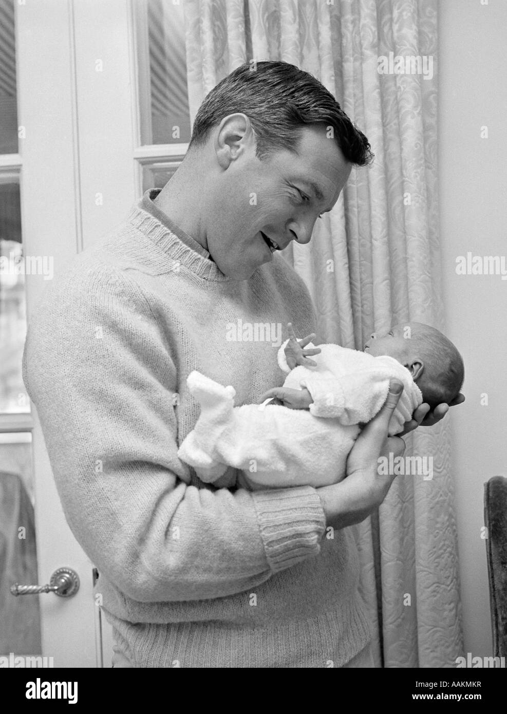 1960 SMILING FATHER HOLDING NEWBORN BABY IN SLEEPER Banque D'Images