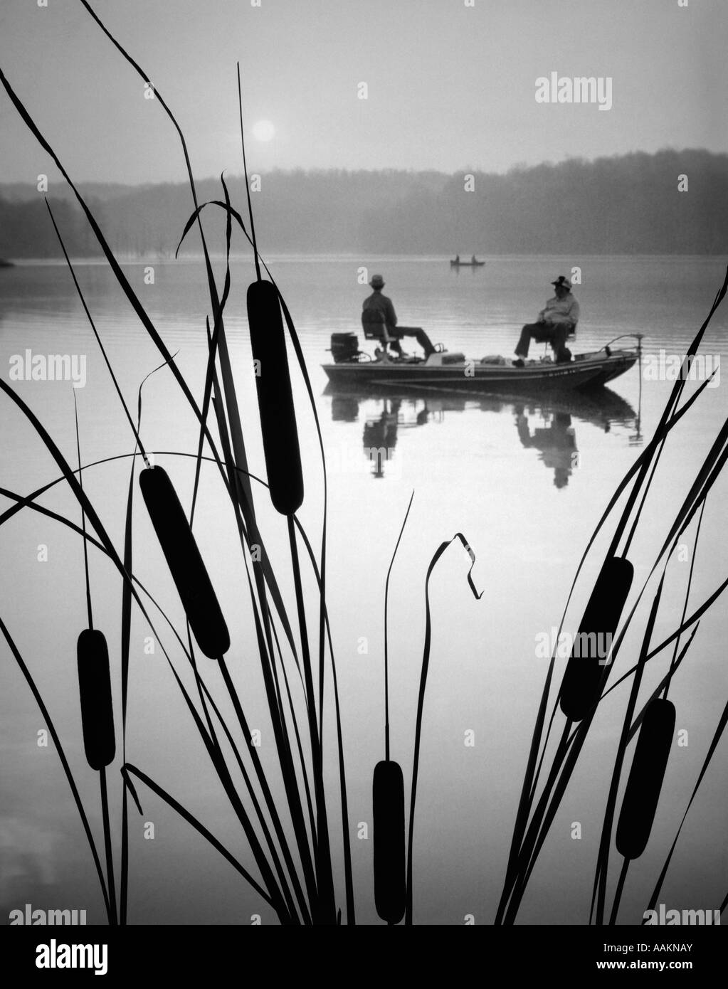 1980 DEUX HOMMES DANS LA PÊCHE BASSE BATEAU SUR L'EAU CALME LAC QUENOUILLES EN PREMIER PLAN Banque D'Images