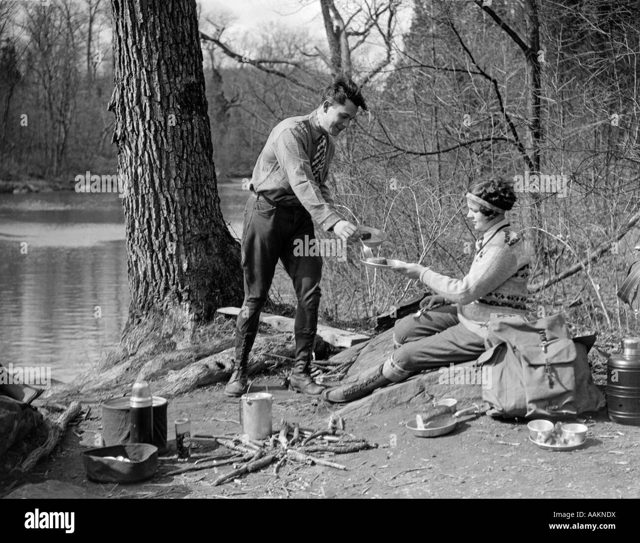 Années 1920 Années 1930 MAN & WOMAN CAMPING PAR LE LAC HAVING PICNIC WOMAN MAN STANDING SERVANT À L'alimentation de l'EST FEMME CREEK SWAMP Banque D'Images