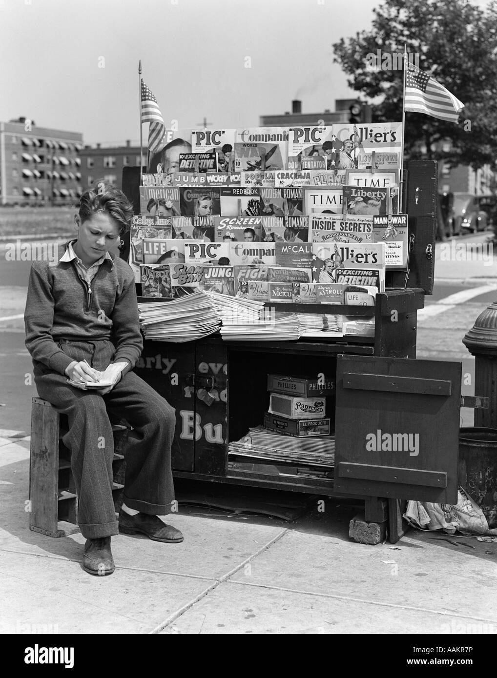 1940 garçon assis AU KIOSQUE À JOURNAUX ÉCRIT DANS LE BLOC-NOTES Banque D'Images