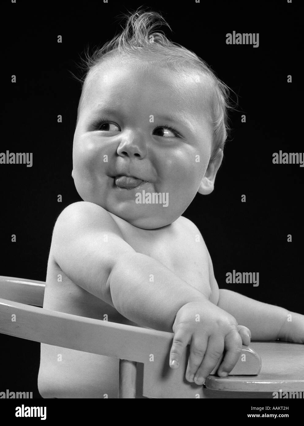 Années 1950 Années 1940 bébé dans une chaise haute tête tournée sur un côté AVEC LA LANGUE QUI SORT L'EXPRESSION DU VISAGE Drôle Banque D'Images