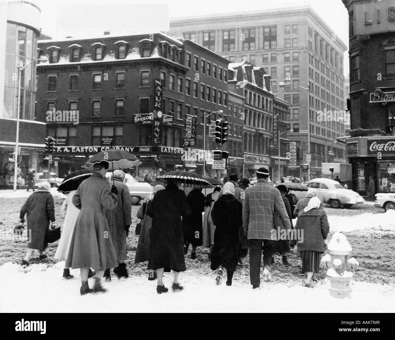 1960 Vue arrière de la petite foule d'hommes & femmes CROSSING CITY STREET À L'INTERSECTION EN HIVER de la neige et de la neige mouillée Banque D'Images