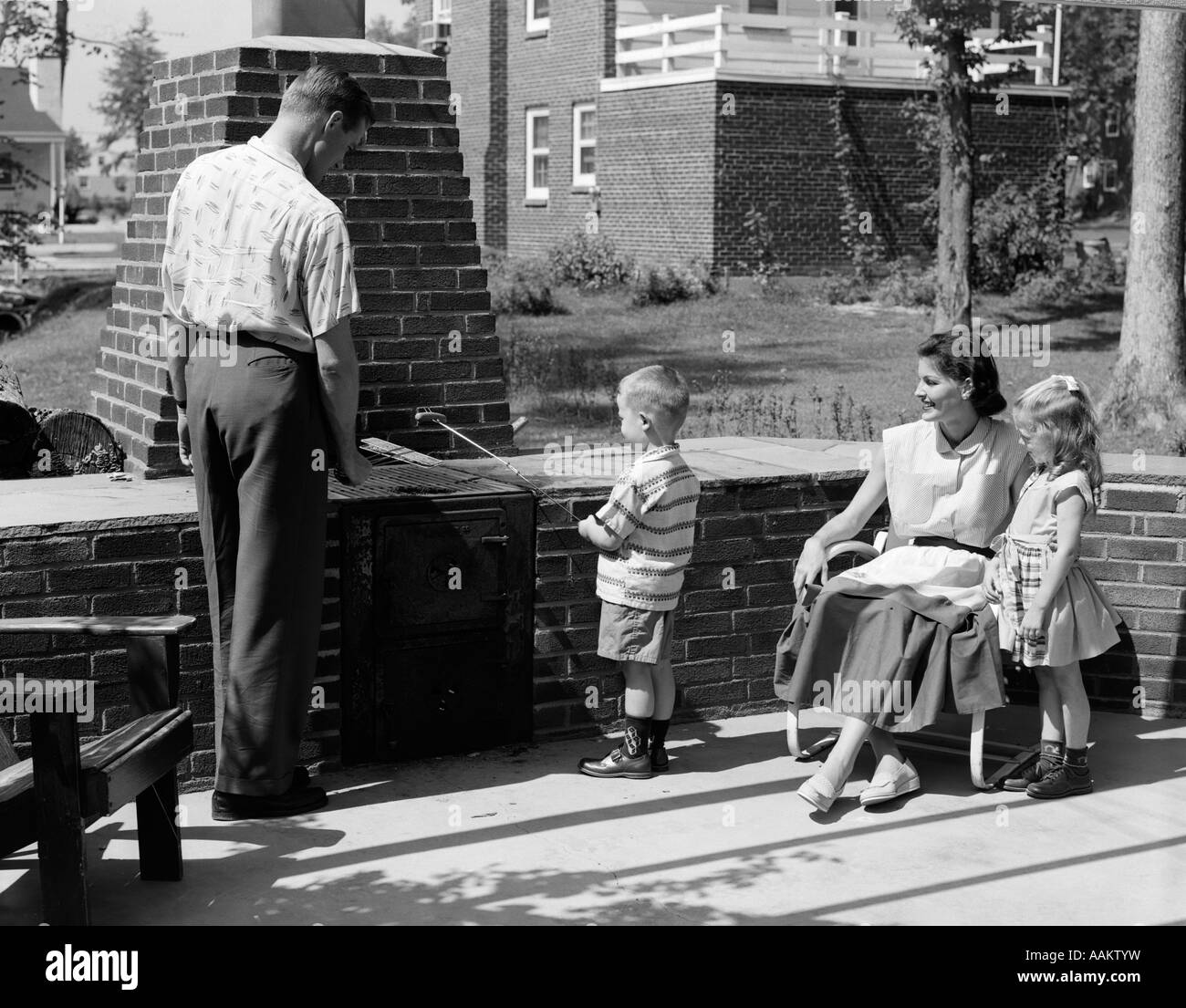 1950 SUR LA FAMILLE MURÉ PATIO DANS L'petit garçon HOT DOG CUISSON SUR BROCHETTE Banque D'Images