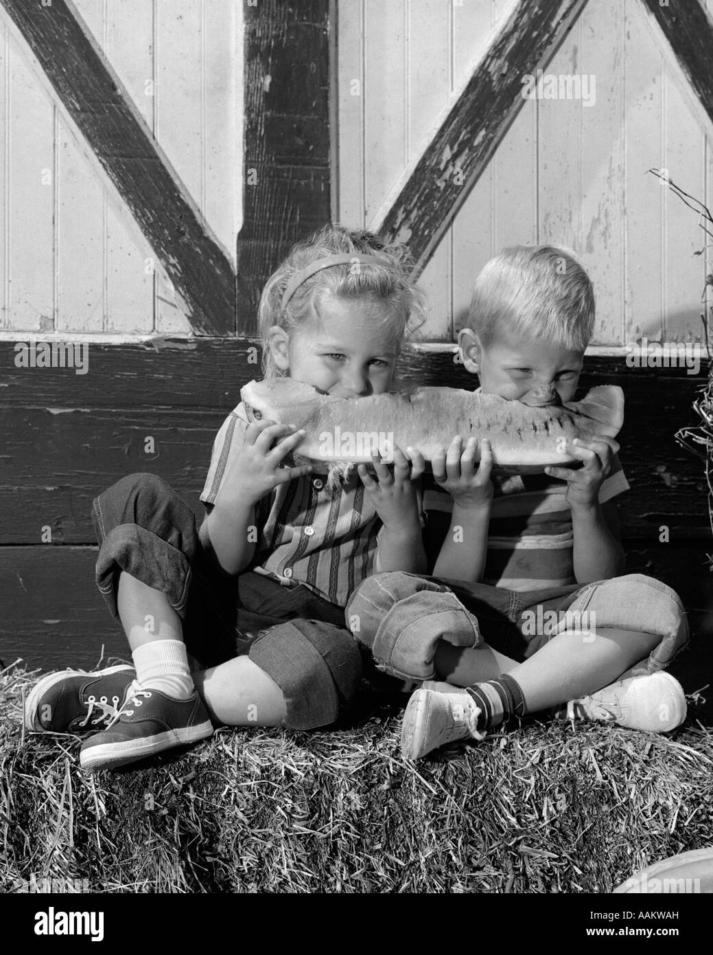 1960 BOY GIRL SITTING ON BALE OF HAY PARTAGE DE LA TRANCHE DE PASTÈQUE LES FRUITS D'ÉTÉ Banque D'Images