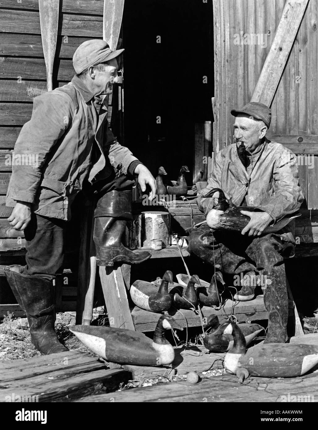 Années 1930 Années 1940 DEUX HOMMES PORTANT DES VÊTEMENTS DE CHASSE EN BOIS RÉPARATION de leurres de BERNACHES DU CANADA BARNEGAT BAY, NEW JERSEY, USA Banque D'Images