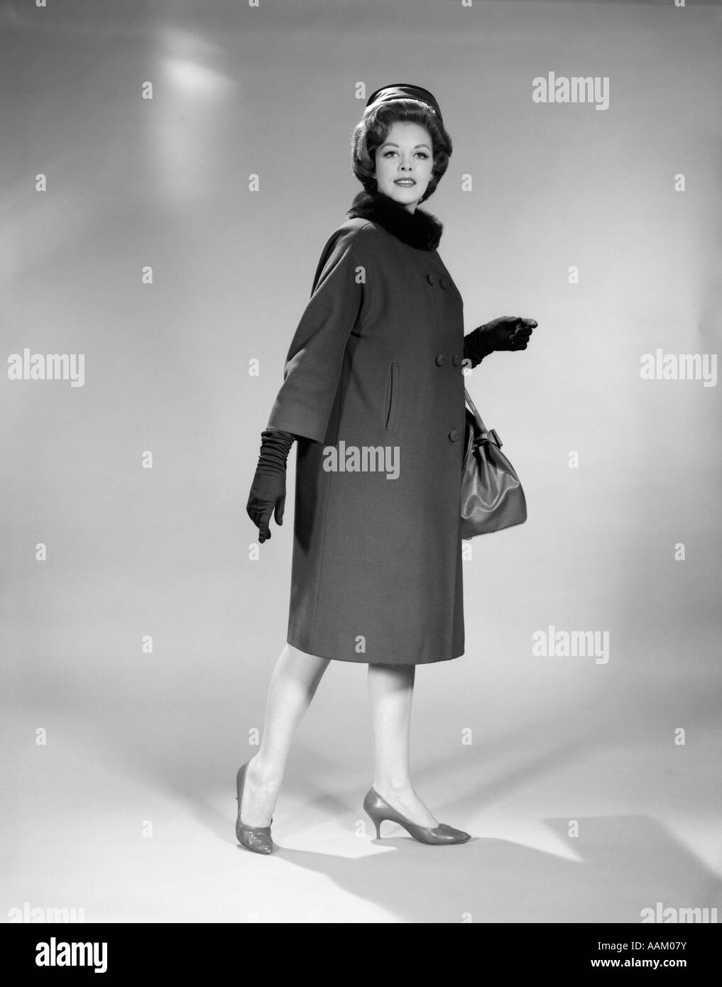 1960 Femme pleine longueur TAMBOURIN HAT MANTEAU Col de Fourrure Gants de sac à main chaussures talon haut STUDIO PORTRAIT LOOKING AT CAMERA Banque D'Images