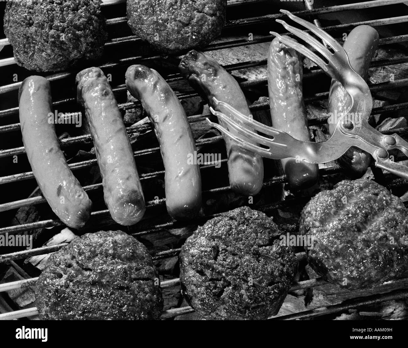 Années 1950, close-up of grill rempli de hot-dogs et des hamburgers et des pinces, descendant jusqu'à les livrer Banque D'Images