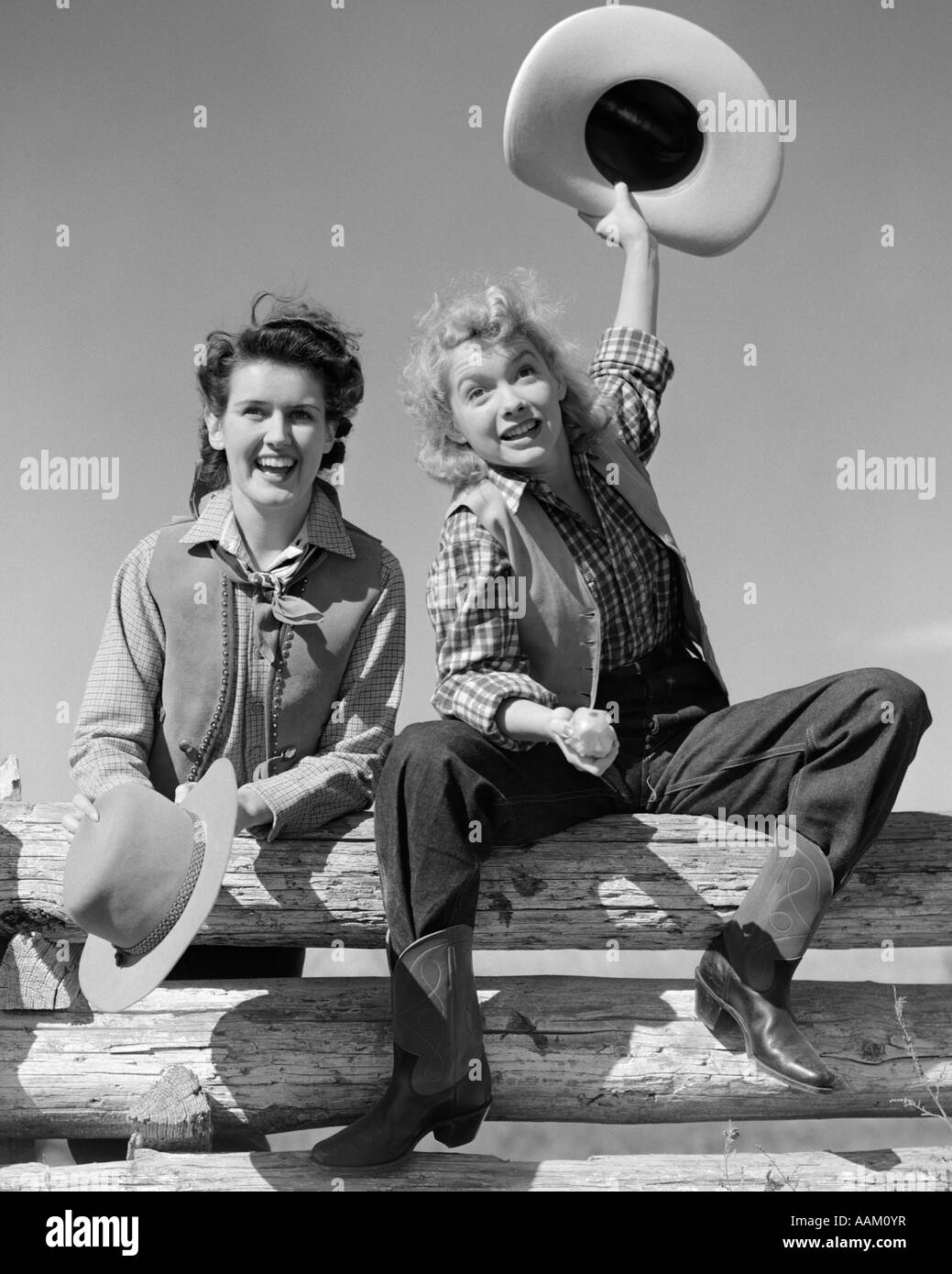 1940 DEUX FEMMES DANS DES TENUES DE COW-BOY SMILING SITTING ON FENCE UNE SENSIBILISATION HAT DANS L'AIR AUTRE se tenait prés d'elle à la fois à la recherche à Banque D'Images