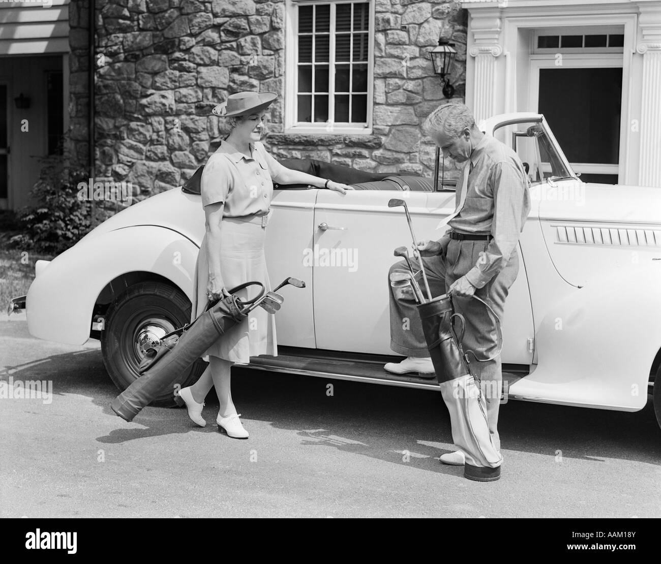 Années 1930 Années 1940 SENIOR COUPLE mettre des bâtons de golf en voiture décapotable PAR STONE HOUSE Banque D'Images