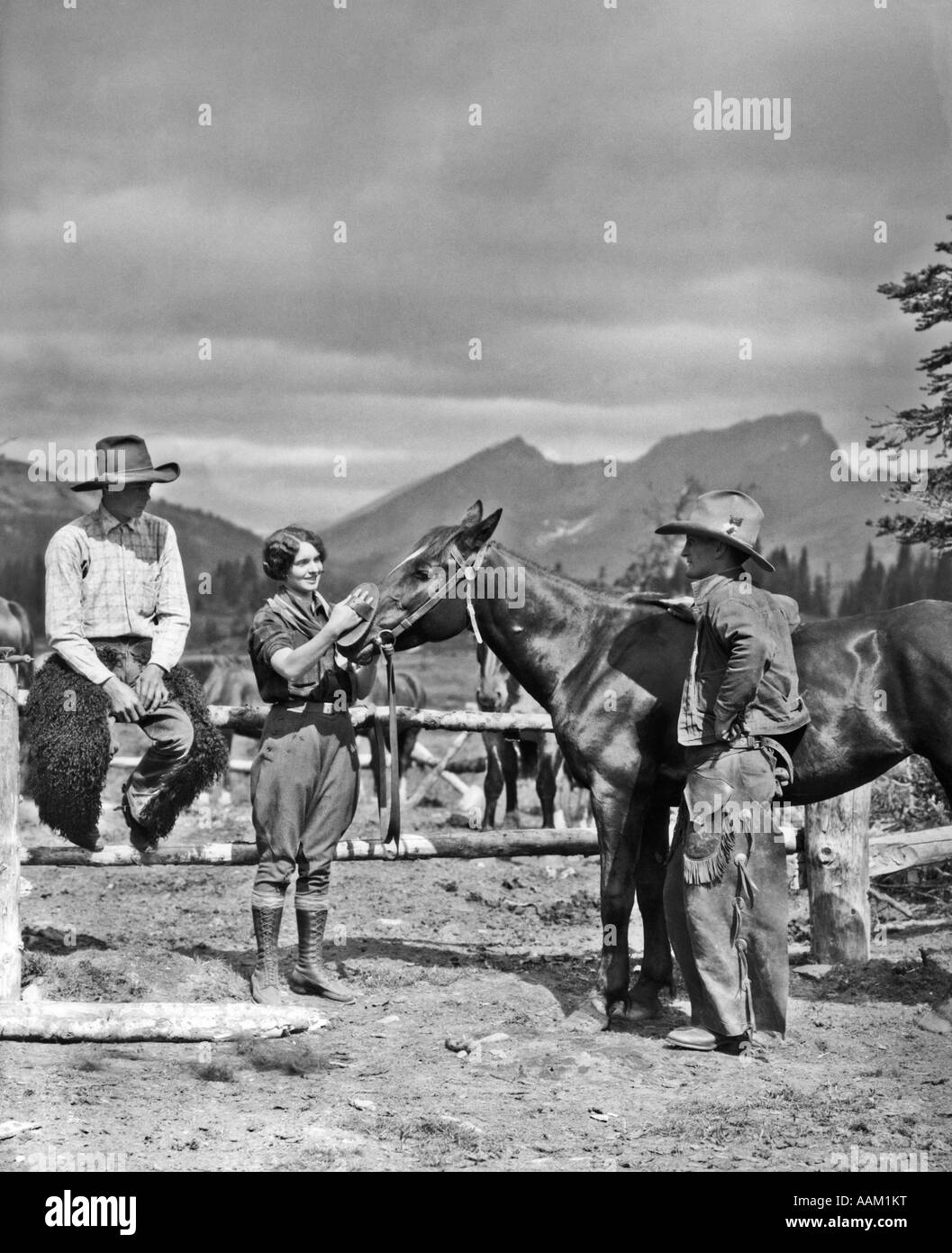 Années 1930 DEUX COWBOYS & TOILETTAGE UNE FEMME UN CHEVAL PRÈS DE L'Enclos le cow-boy est debout portant des CHAPS BATWING Banque D'Images