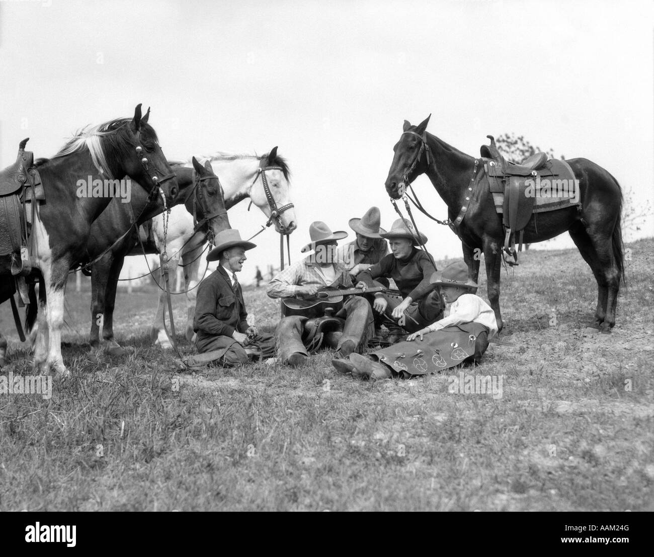 Années 1920 1930 GROUPE DE 5 COWBOYS SITTING PAR LEURS CHEVAUX L'UN DÉTIENT LE CHANT GUITARE Banque D'Images