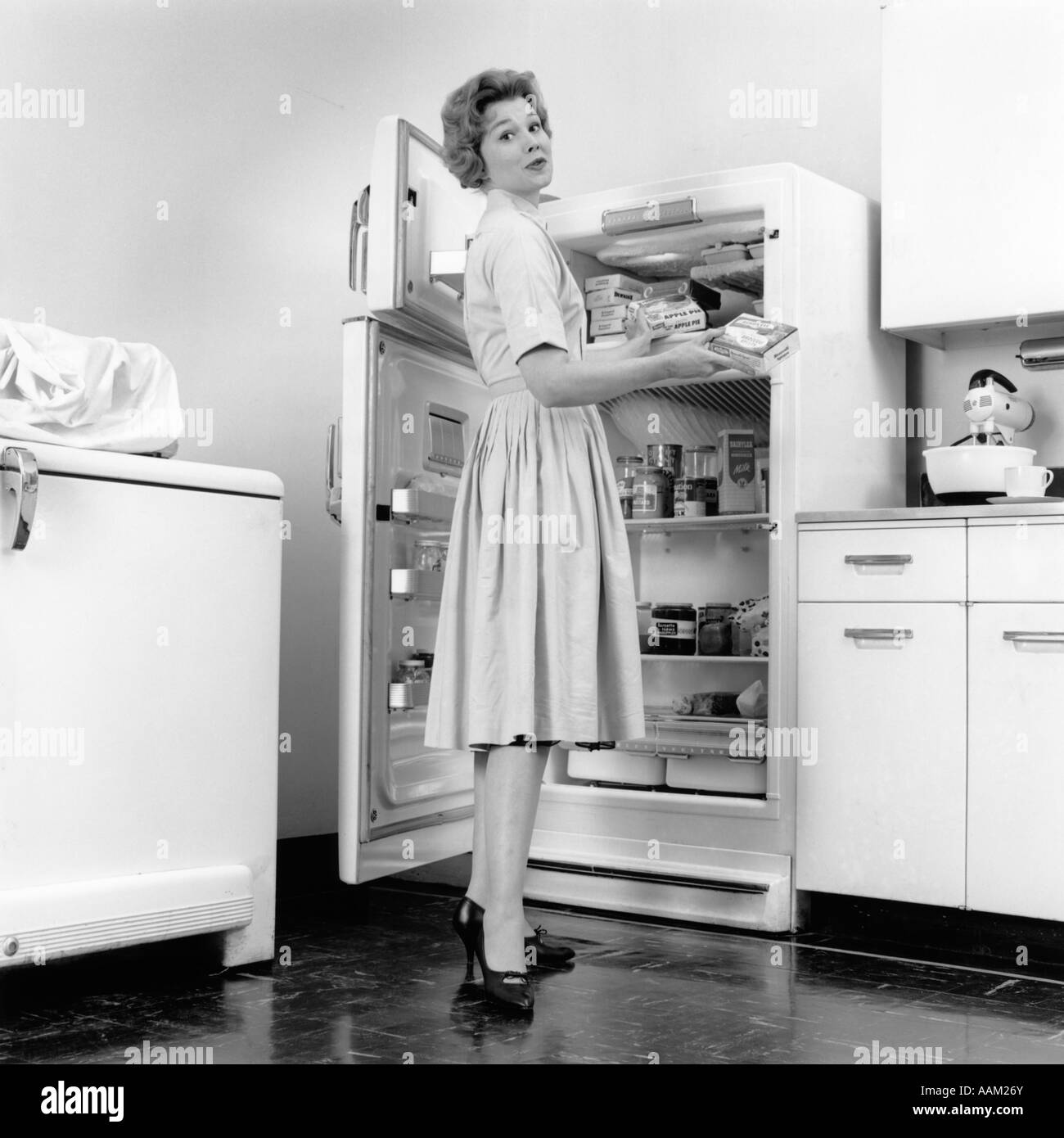 1950 FEMME DEBOUT DANS LA CUISINE D'un réfrigérateur Banque D'Images