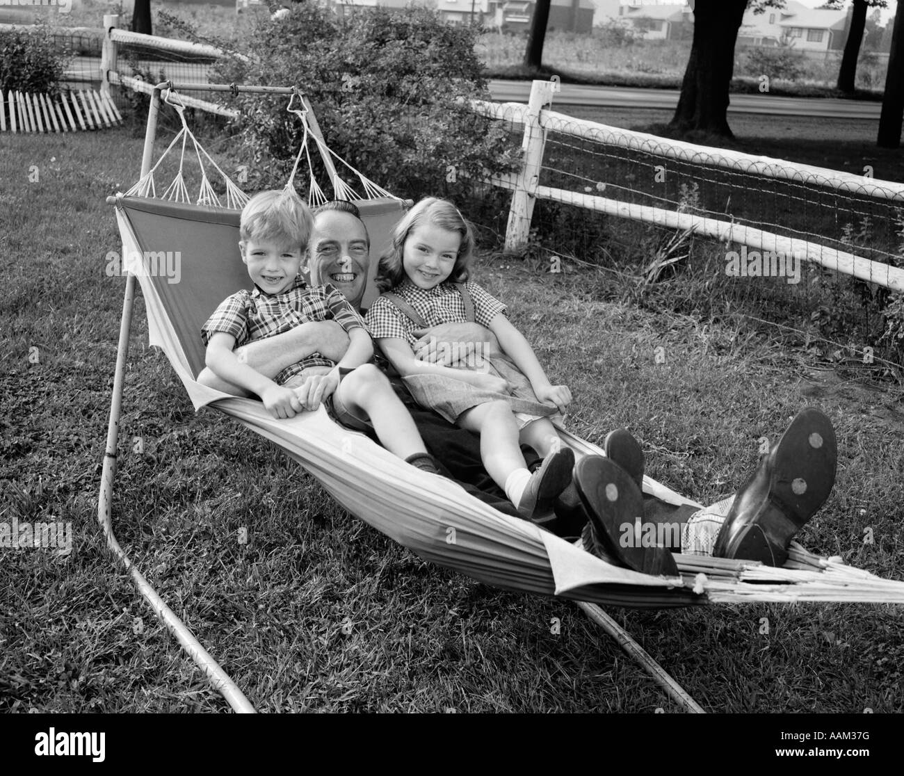 1950 Père couché dans un hamac HOLDING Smiling Children 2 Garçon Fille Banque D'Images