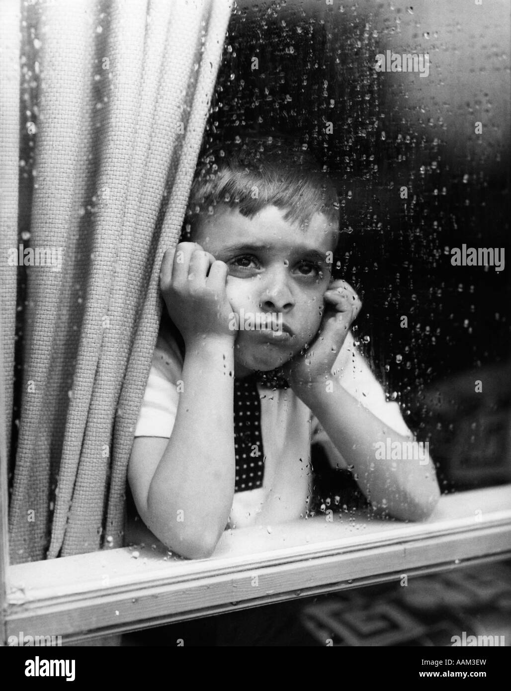 1950 SAD BOY À L'EXTÉRIEUR À TRAVERS LA FENÊTRE LA PLUIE Banque D'Images