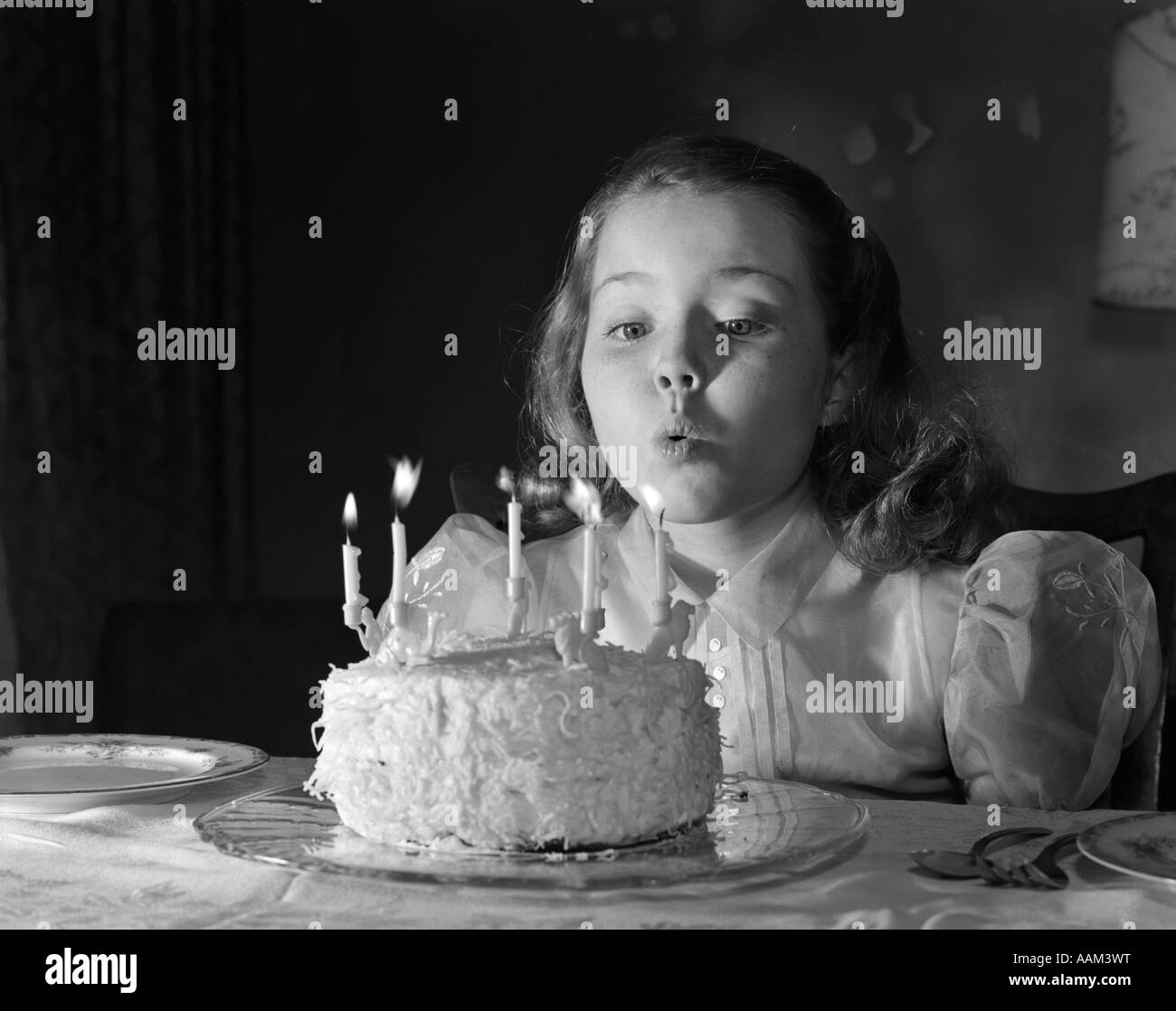 1950 FAIRE UN VOEU PETITE FILLE DE CINQ ANS souffler les bougies du gâteau d'anniversaire Banque D'Images