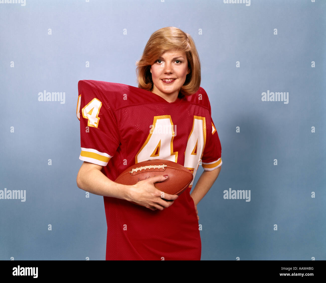 1970 FEMME EN ROUGE DE TAILLE MOYENNE PLUS DE NUMÉRO DE MAILLOT DE FOOTBALL 44 PORTANT ÉPAULETTES HOLDING SPORTS DE BALLE L'HISTOIRE Banque D'Images