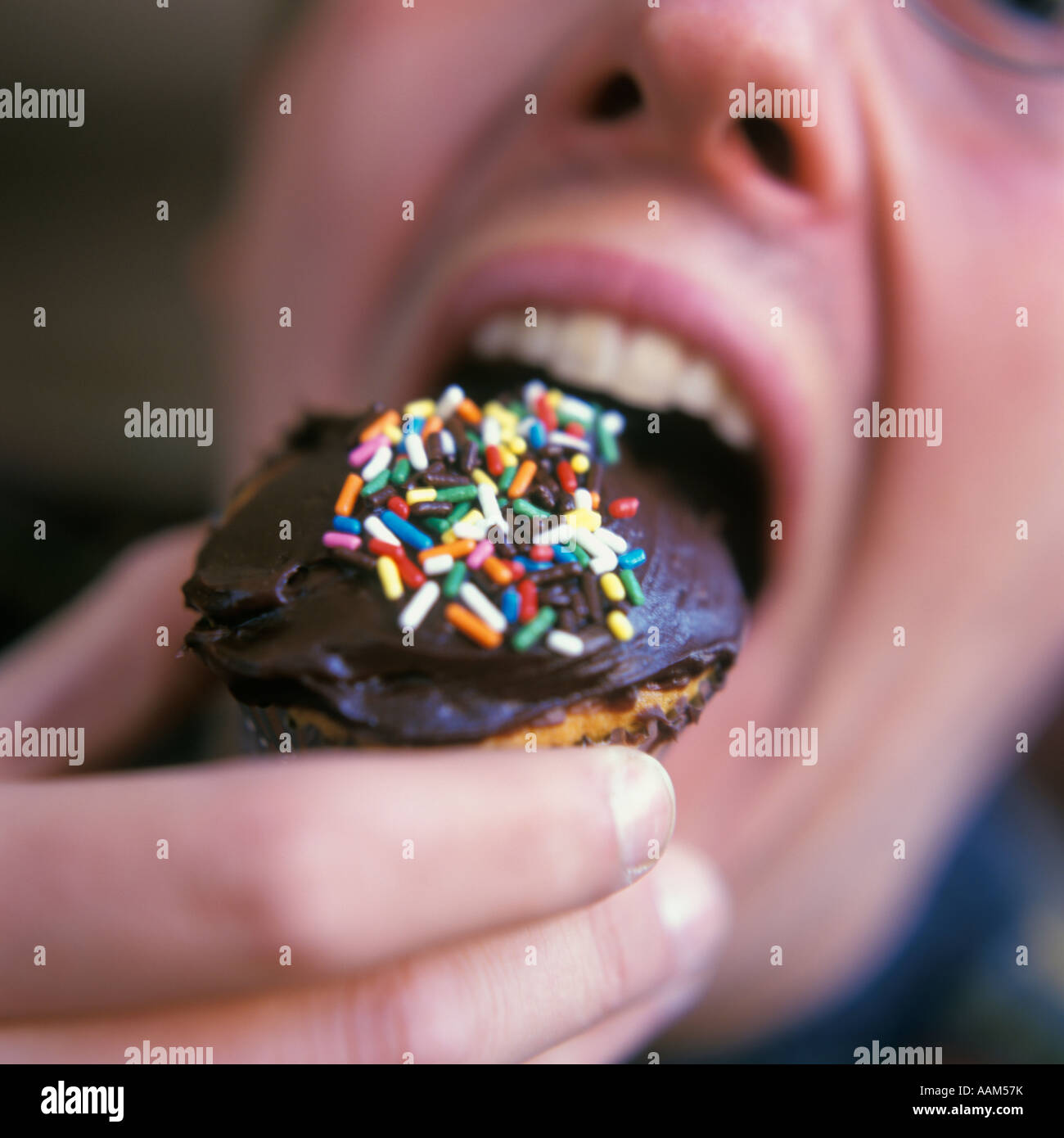 CLOSE-UP MAN EATING CUPCAKE AVEC GLAÇAGE AU CHOCOLAT ET MULTICOLORE JIMMIES Banque D'Images