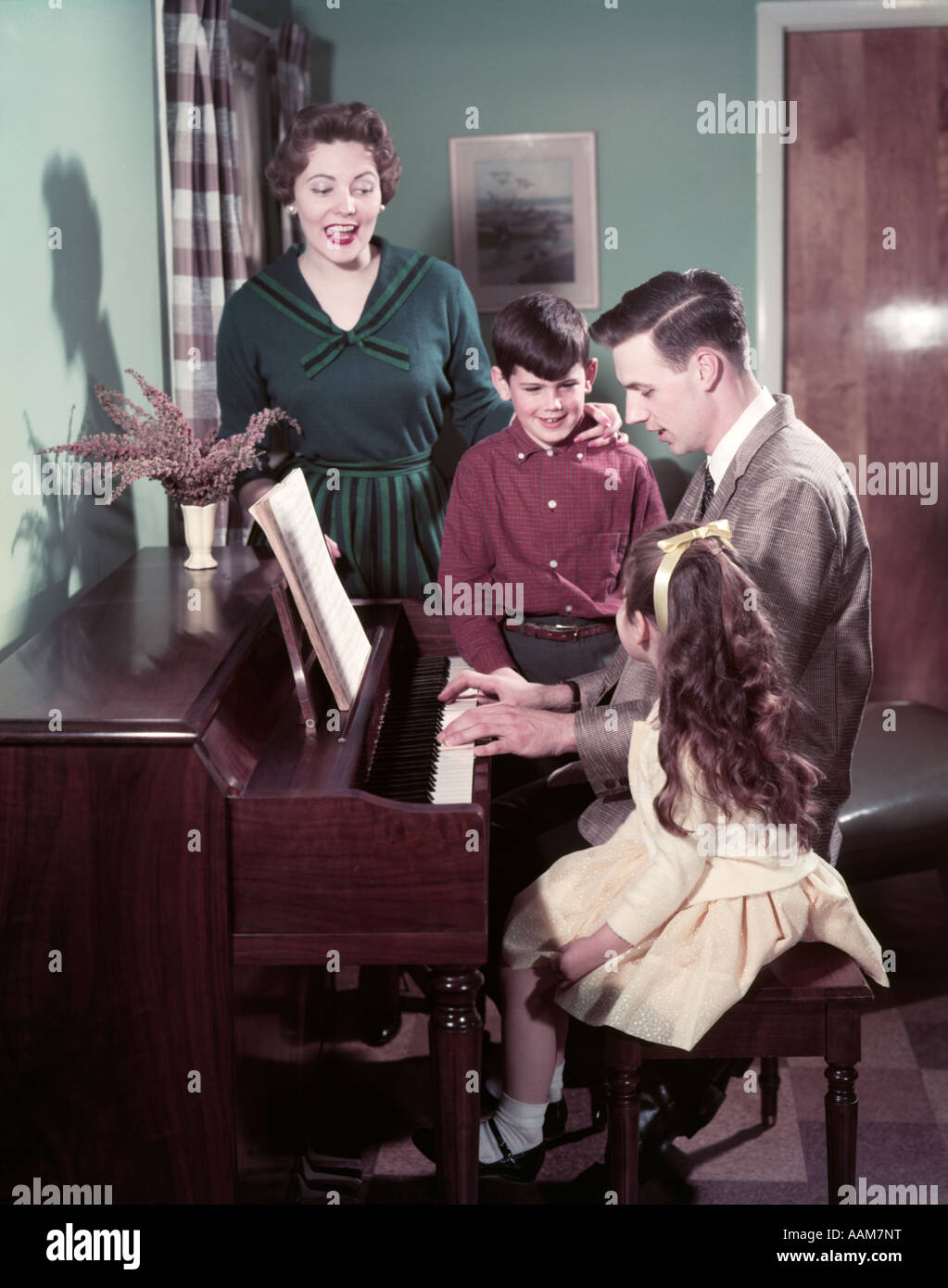 1950 FAMILLE 4 PÈRE JOUER DU PIANO L'HOMME FEMME Garçon Fille Mère Fils Fille CHANTER DEBOUT BANC DE VASE DE SALON Banque D'Images