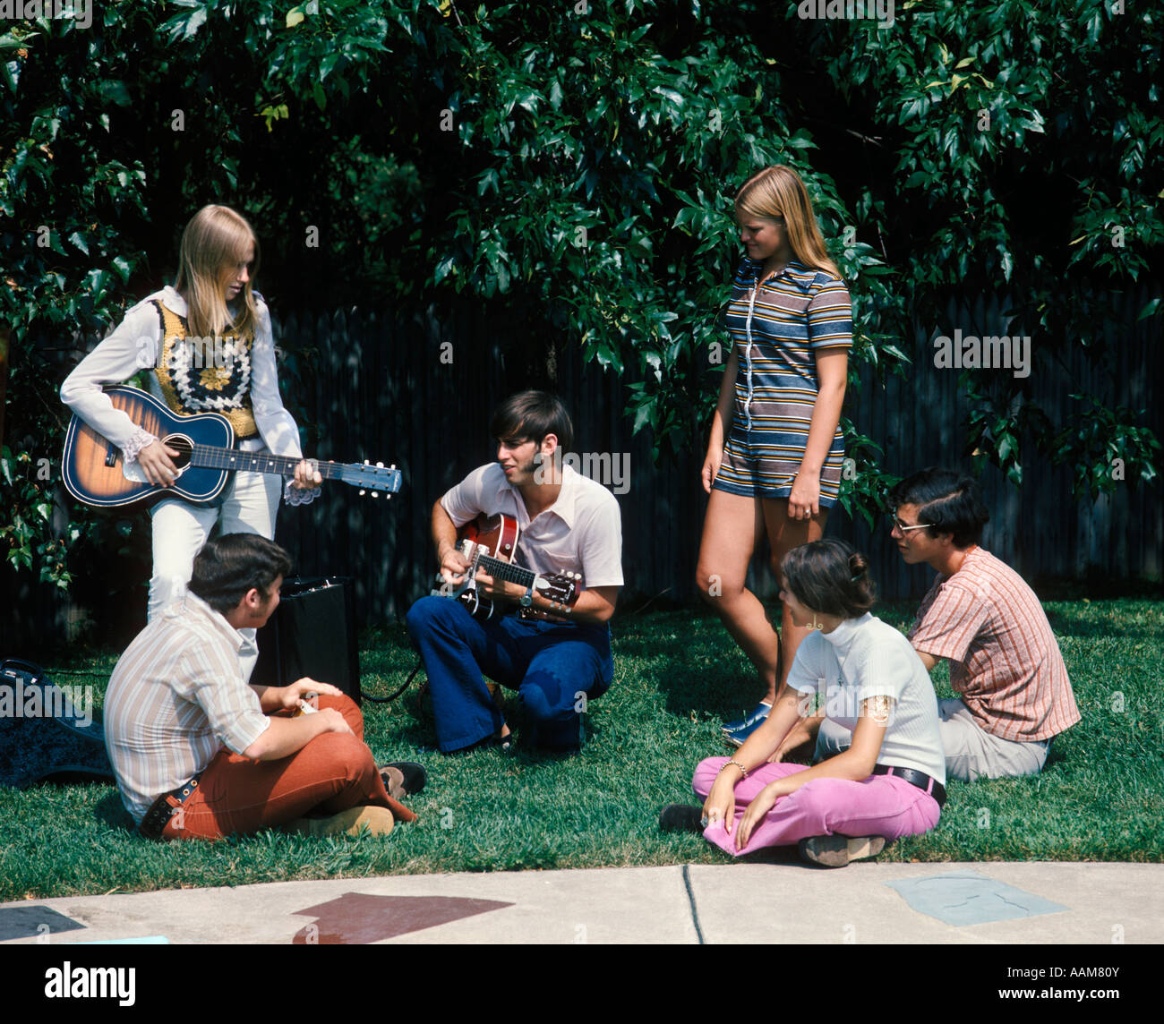 1960 1970 GROUPE DE 6 adolescents Garçons Filles dans la cour de l'été 1 Garçon 1 FILLE QUI JOUE DE LA GUITARE DES FAVORIS FASHION Banque D'Images