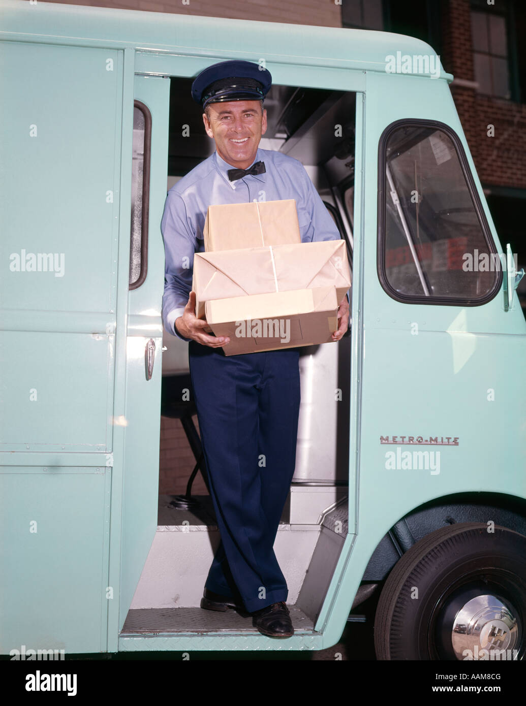 1960 SMILING DELIVERY MAN CARRYING PILE DE PAQUETS À L'INTENSIFICATION DE L'ÉTAPE DE PORTE CONDUCTEUR VAN DE L'OCCUPATION Banque D'Images