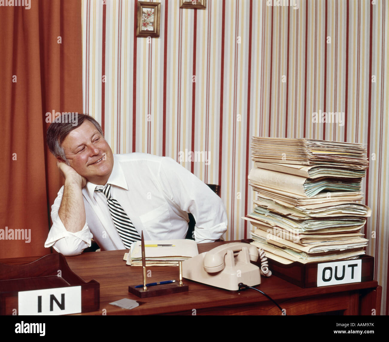 Années 1960 Années 1970 SMILING HAPPY OFFICE WORKER HOMME GREFFIER Exécutif siègent au Bureau CHERCHER À PLEIN LE BAC et dans le bac vide Banque D'Images