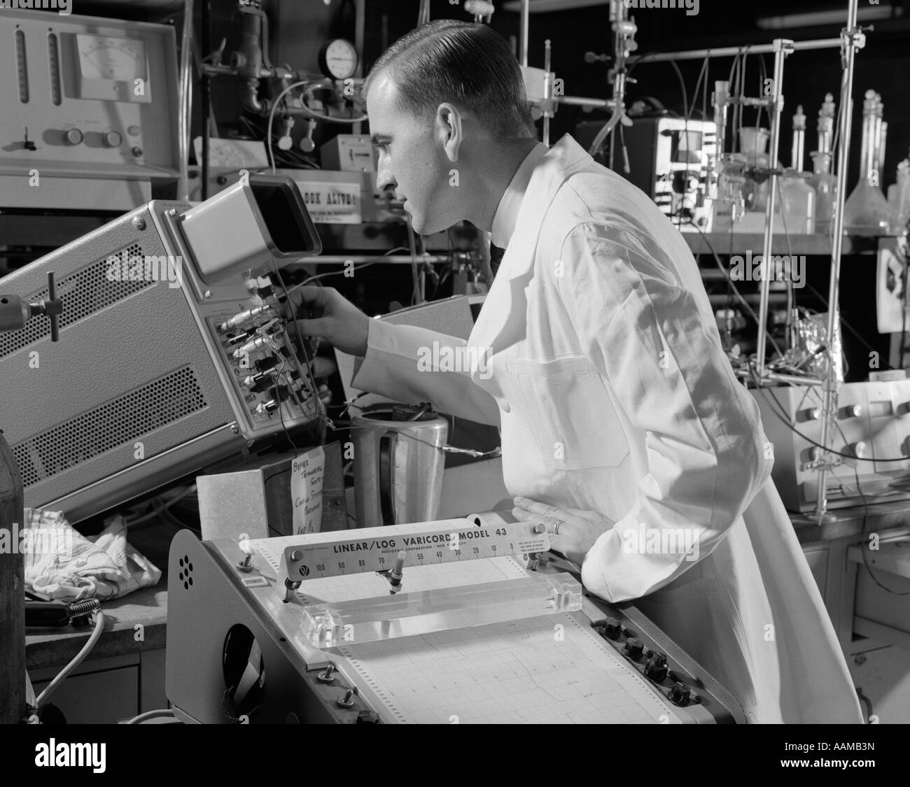 1960 TECHNICIEN DE LABORATOIRE MÂLE VÊTU D'UN SARRAU BLANC LA LECTURE D'UN OSCILLOSCOPE Banque D'Images