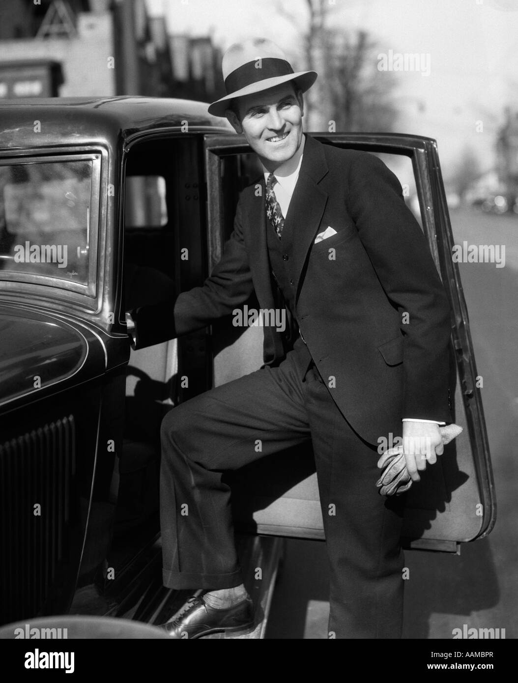1930 SMILING MAN IN SUIT ET GANTS HAT HOLDING FAISANT UN PAS DANS LE SIÈGE DU PILOTE AUTOMOBILE Banque D'Images