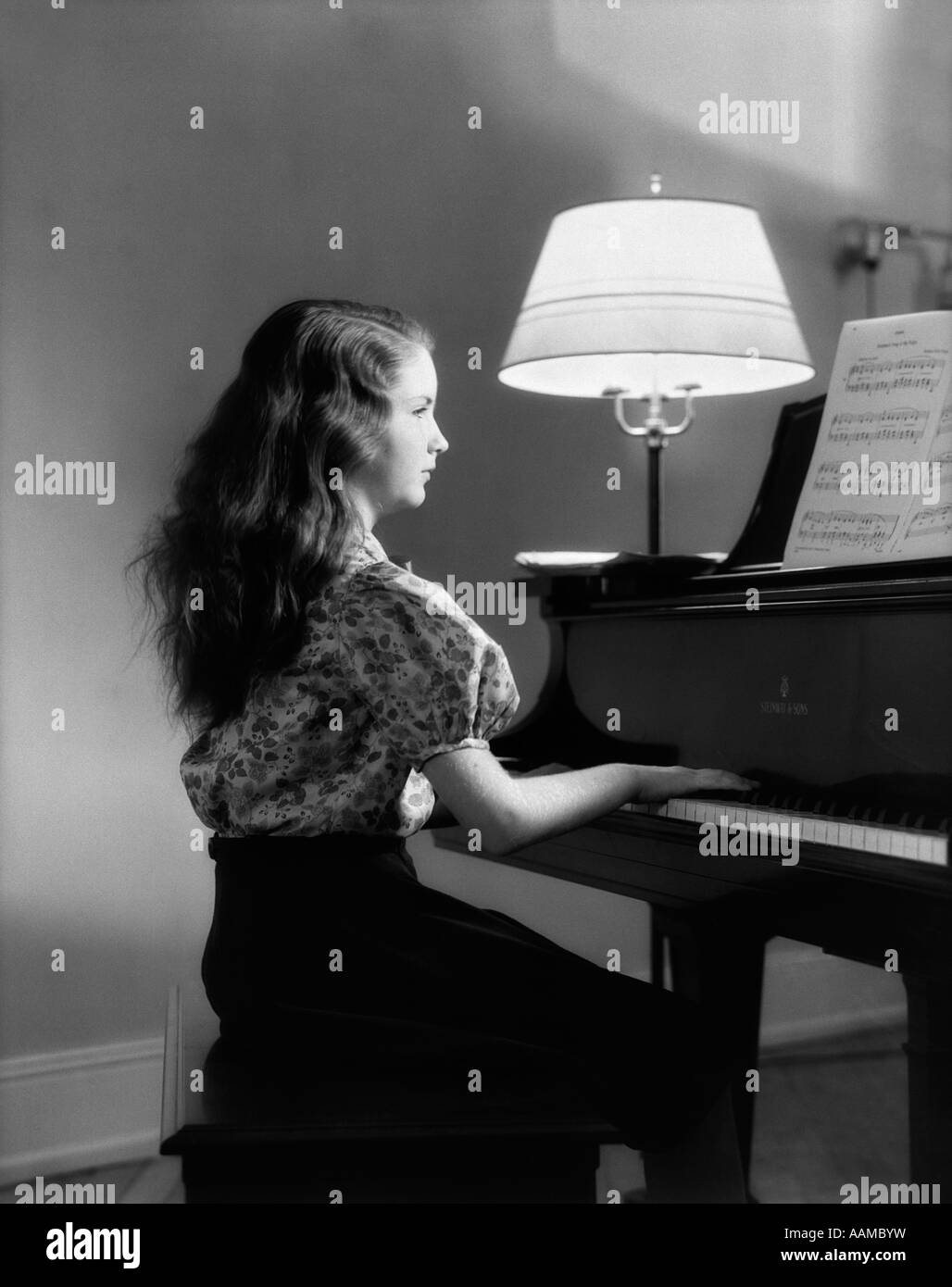 1930 VUE DE CÔTÉ GIRL PLAYING PIANO AVEC LAMPE ALLUMÉE À CÔTÉ D'ELLE Banque D'Images